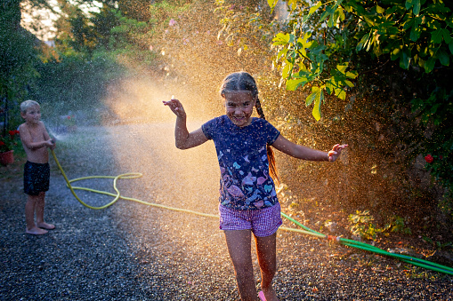 Joyful kids play with water hose in summer light, splashing and laughing in a backyard, creating memories in the golden hour sunlight.