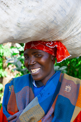 May 2017, Kinigi, Rwanda: Portrait of a African woman outdoors  carrying a bag on her head.