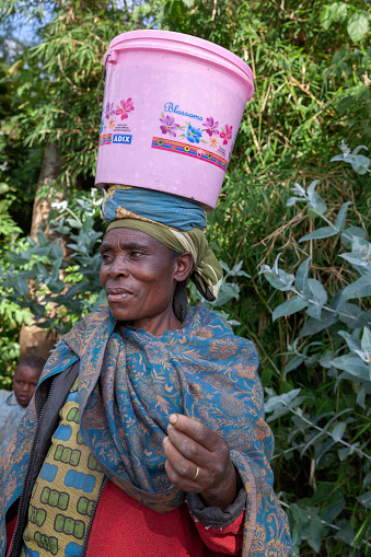 May 2017, Kinigi,, Rwanda: Portrait of a African woman outdoors carrying a bucket on her head.