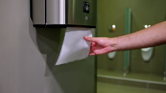 At the public restroom, unrecognizable young Caucasian man using paper towel to dry his hand