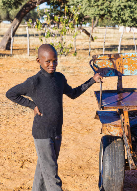 bambino africano sorridente in piedi accanto a un carro arrugginito dell'asino nel villaggio al tramonto, - community outreach social worker teenager poverty foto e immagini stock