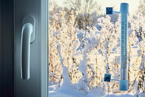 Air temperature is 20 degrees below zero Celsius on scale of an outdoor thermometer, fixed to window glass with adhesive tape on  outside.