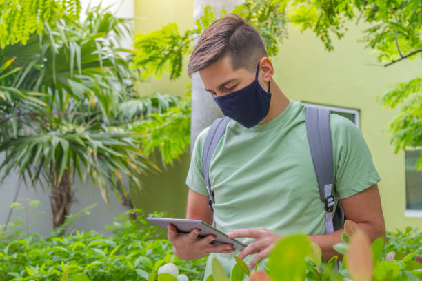 porträt eines jungen, gutaussehenden studenten, der einen rucksack trägt und ein digitales tablet in der hand hält, während er auf dem universitätscampus vor der bibliothek mit 5g-technologie im internet surft. - library student latin american and hispanic ethnicity university stock-fotos und bilder