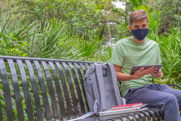 porträt eines jungen, gutaussehenden studenten, der einen rucksack trägt und ein digitales tablet in der hand hält, während er auf dem universitätscampus vor der bibliothek mit 5g-technologie im internet surft. - library student latin american and hispanic ethnicity university stock-fotos und bilder