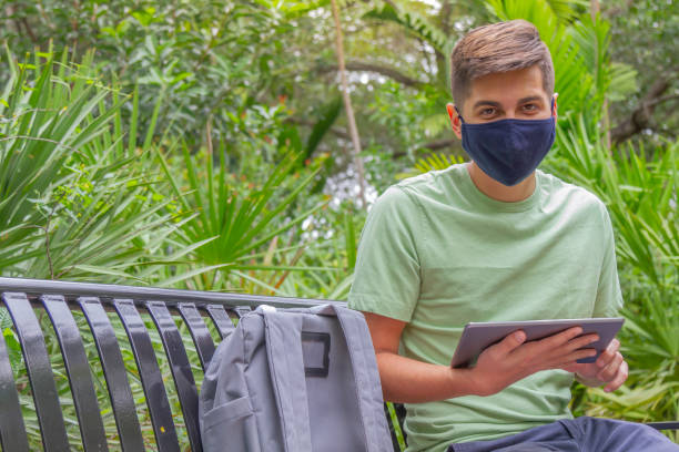 porträt eines jungen, gutaussehenden studenten, der einen rucksack trägt und ein digitales tablet in der hand hält, während er auf dem universitätscampus vor der bibliothek mit 5g-technologie im internet surft. - library student latin american and hispanic ethnicity university stock-fotos und bilder