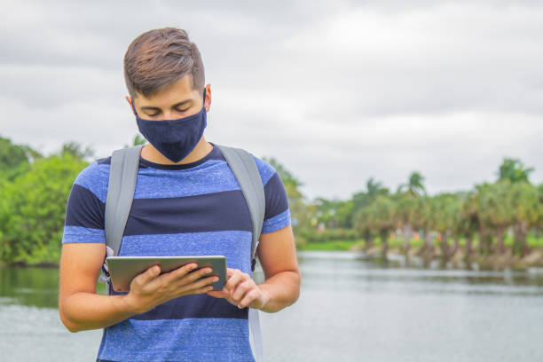 porträt eines jungen, gutaussehenden studenten, der einen rucksack trägt und ein digitales tablet in der hand hält, während er auf dem universitätscampus vor der bibliothek mit 5g-technologie im internet surft. - library student latin american and hispanic ethnicity university stock-fotos und bilder