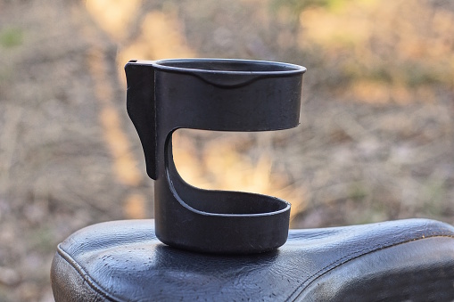 one empty black plastic cup holder stands on a leather bicycle saddle on the street on a gray background