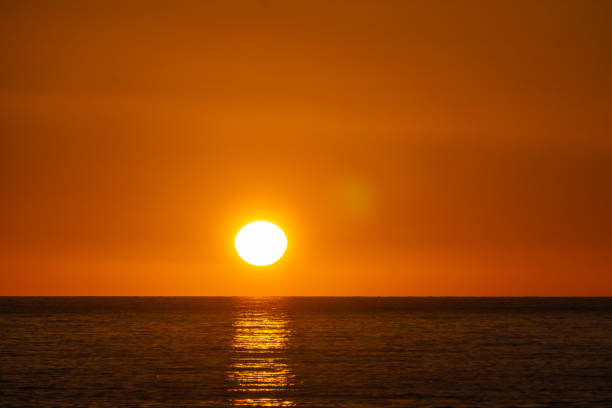 Bright sunset with large yellow sun on orange sky with sea surface underneath