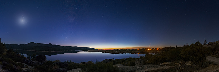 Panorama of nigh sky with Crescent moon and planets Venus, Saturn, Jupiter and Milky Way over lake, Vale do Rossim, Serra da Estrela, Portugal
