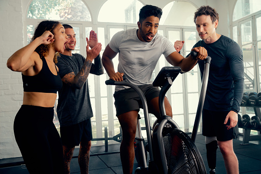 Multiracial young adults wearing sports clothing motivating friend cycling on exercise bike at the gym