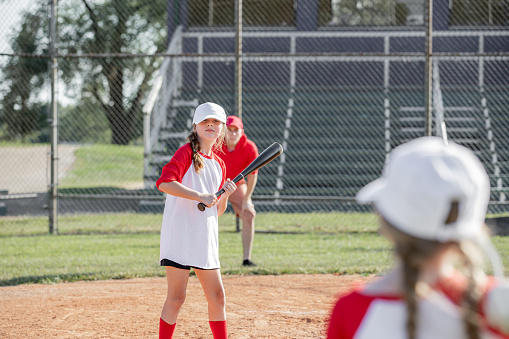 Elementary school-aged athletes, both boys and girls, engage in co-ed little league baseball, supported by their coaches on the vibrant ballfield