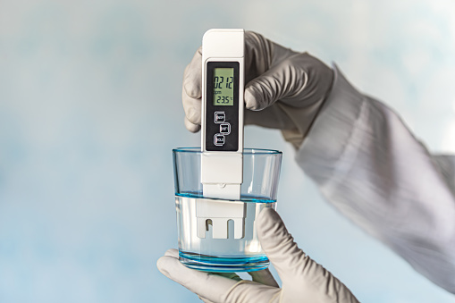 pH meter in hands with gloves, glass of water on a blue background. Measurement of the characteristics of drinking water. The hardness of the water. poor water quality. high values of salt impurities