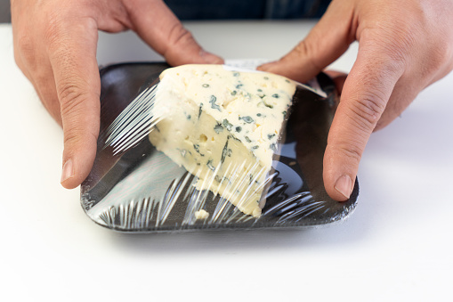 Blue cheese gorgonzola in plastic packaging on white background. cheese with blue mold in men hands