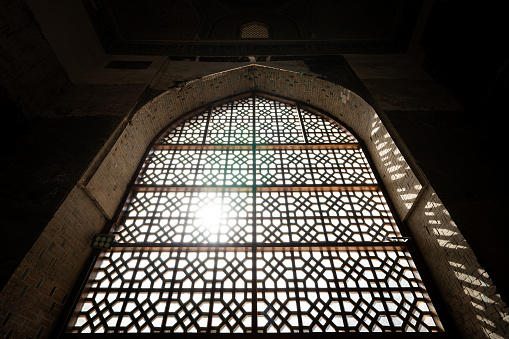 Oriental style window with bar and sun shining through it. the grille on the window. Traditional Islamic style in the architecture and interior of the Middle East
