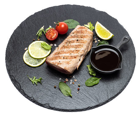 grilled cooked piece of tuna fillet on black stone serving board.