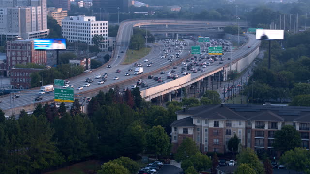 Winding highway with busy traffic leading to Downtown of Atlanta, Georgia. Contrast between detached residential houses and high buildings in the distance.  Aerial footage with panning camera motion