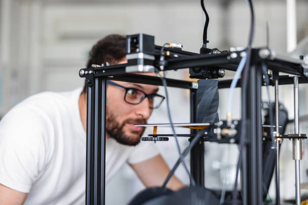 young male designer wearing glasses is looking with attention a 3d printer to check how it - Unleash Your Creativity with Miniatures 3D Printing