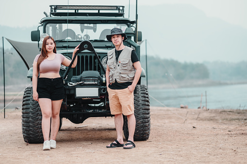 Confident couple stands proudly by their car at a campsite, showcasing their adventurous spirit and readiness for outdoor exploration.