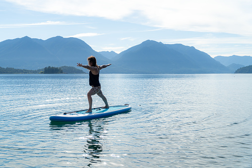 Woman doing yoga in a stand up paddle board in a summer morning in the lake.