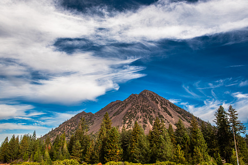 Mount Shastina on a partly cloudy day and blue sky, viewed from close, with coniferous trees at the base and large blue sky copy space