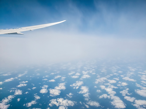 Cloud patterns with airplane flying between layers. Features plane wingtip. View through the cabin window.