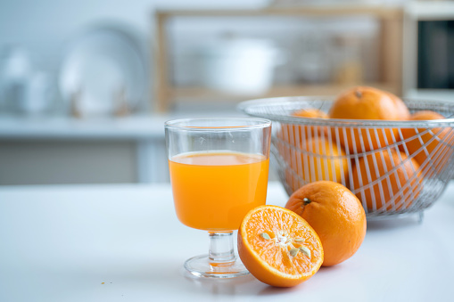 Orange fruits and a glass of orange juice are on the table for breakfast in the home kitchen, selective focus