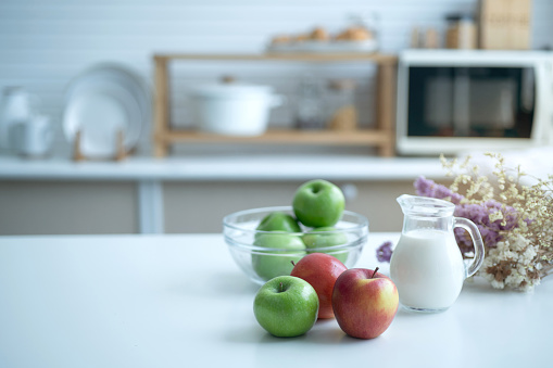 Red and green apples are on the table with a pitcher of milk prepared for breakfast in the home kitchen, selective focus