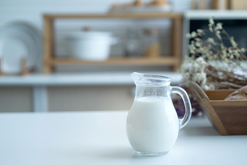 Pitcher of milk prepared for breakfast is placed near a basket of baked bread in the home kitchen, selective focus
