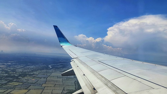 Airplane wing over urban landscape with dramatic cloudscape, viewed from cabin window during flight.