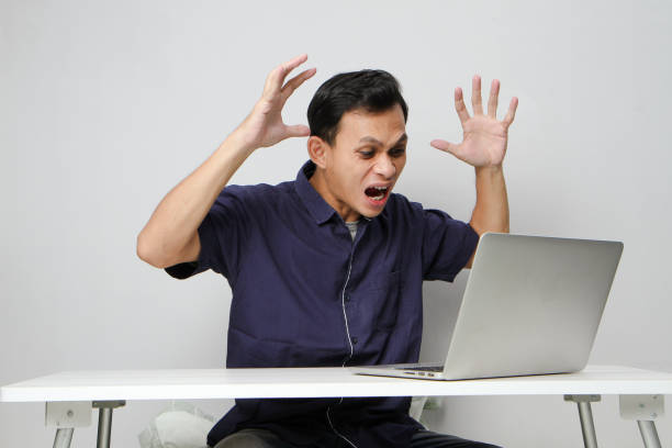 istock Angry mad asian man in workplace while sitting in front of laptop computer. isolated background 2129075020