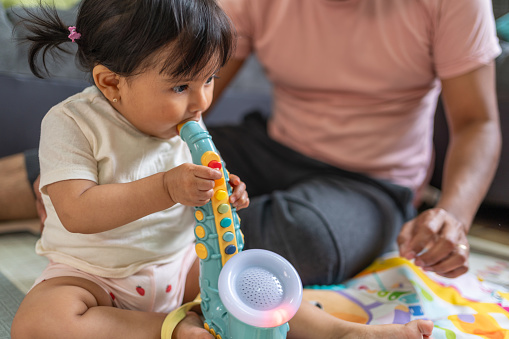 Hispanic father and daughter playing with musical toys in the living room, latin toddler happily playing a toy saxophone, joyful family bonding moment