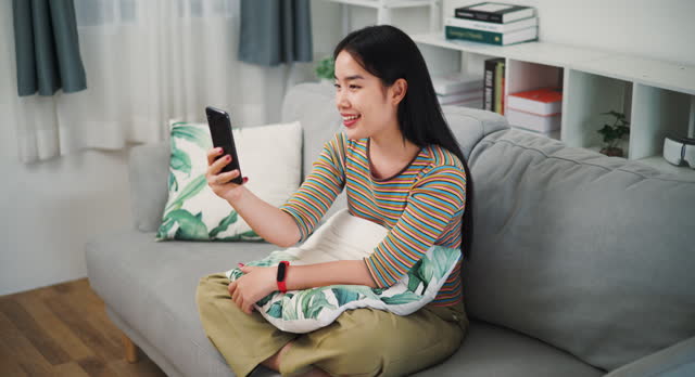 Young woman talking on the phone laughing happily on the sofa at home.