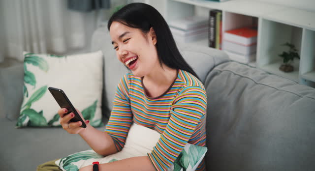 Young woman talking on the phone laughing happily on the sofa at home.