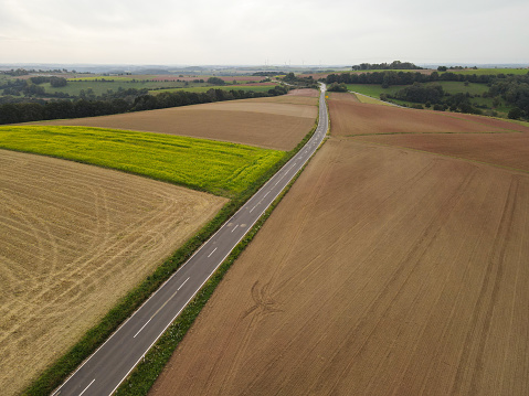 View from above of a long rural asphalt road between farm fields in the countryside