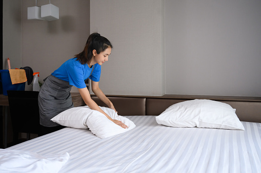 Happy young woman making bed after wake up. Housework, hygiene and lifestyle concept.