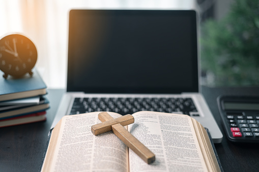 Cross on bible and laptop in online study bible concept. Holy Bible concept for modern religious education, podcast or help with hearing for blind studying