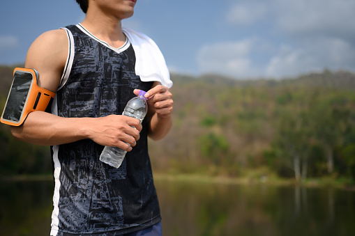 Active sportsman holding a bottle of water taking a break during morning workout.