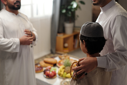 Selective focus shot of proud Muslim father and his son talking to male relative at family gathering on Eid Al-Fitr, copy space