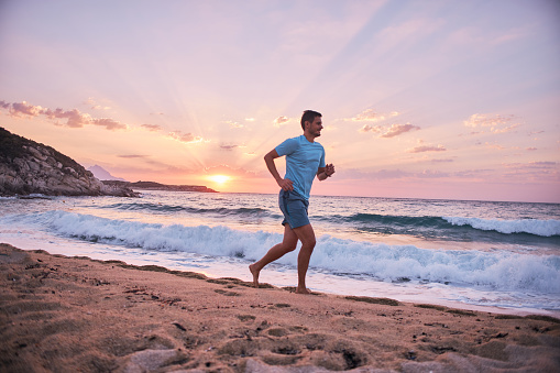 Active man running on the beach at sunset.
