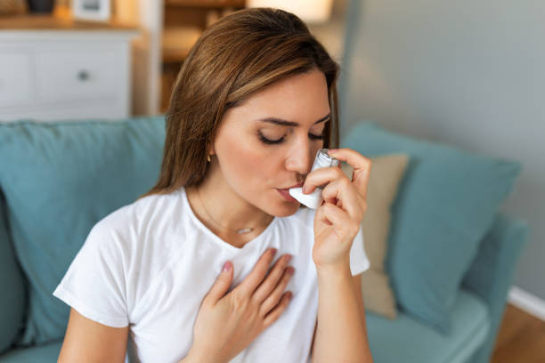 istock Woman using inhaler while suffering from asthma at home. Young woman using asthma inhaler. Close-up of a young woman using asthma inhaler at home. 2129334096