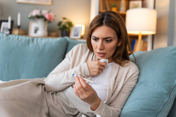 istock Sickness, seasonal virus problem concept. Woman being sick having flu lying on sofa looking at temperature on thermometer. Sick woman lying in bed with high fever. Cold flu and migraine. 2129334111
