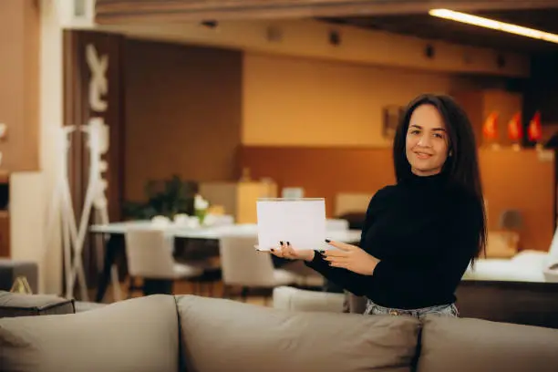 Photo of A woman seller of sofas with a white sign in her hands in a furniture store