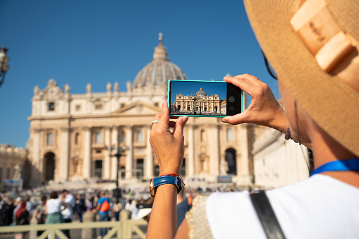 Women takes a photo with a smartphone of the St. Peter's Basilica in Vatican City, Rome, Italy