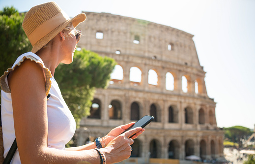 Woman tourist sitting and resting in front of Coliseum and using smart phone Rome, Italy