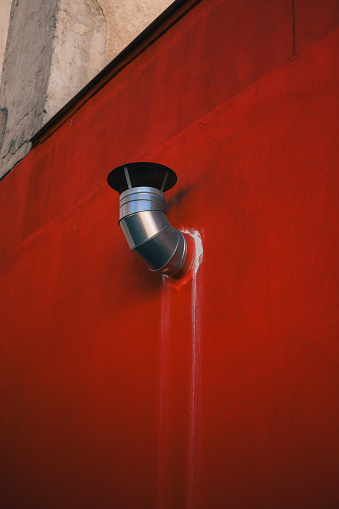 Smoke billows from a pipe on a red wall near a building