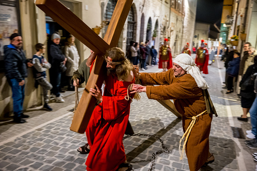 Gualdo Tadino, Umbria, Italy, March 29 -- Celebrations in period costume of Holy Week and Easter in a medieval village in Umbria, in central Italy. In the photo: A man represents Jesus Christ during the Stations of the Cross procession (Via Crucis), carrying the Cross along the alleys and streets of the town. The Umbria region, considered the green lung of Italy for its wooded mountains, is characterized by a perfect integration between nature and the presence of man, in a context of environmental sustainability and healthy life. In addition to its immense artistic and historical heritage, Umbria is famous for its food and wine production and for the high quality of the olive oil produced in these lands. Image in high definition quality.