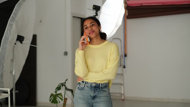 Beauty young photographer talking to the mobile phone standing in her studio