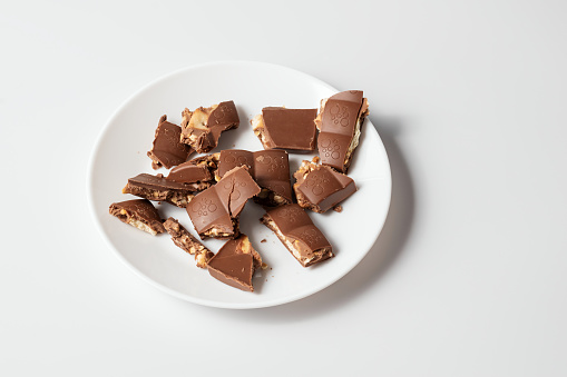 Milk chocolate on a white background. Chocolate bar broken into pieces on white plate