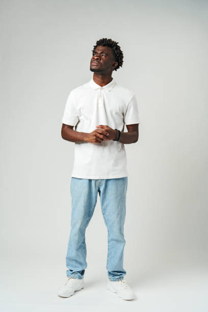 istock Young Man in Casual Clothing Standing Against a Plain Background With a Contemplative Expression 2129464355
