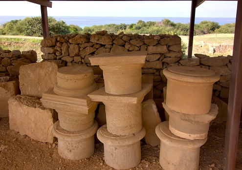 Parts of ancient columns and stone blocks stacked under a canopy at the archaeological site
